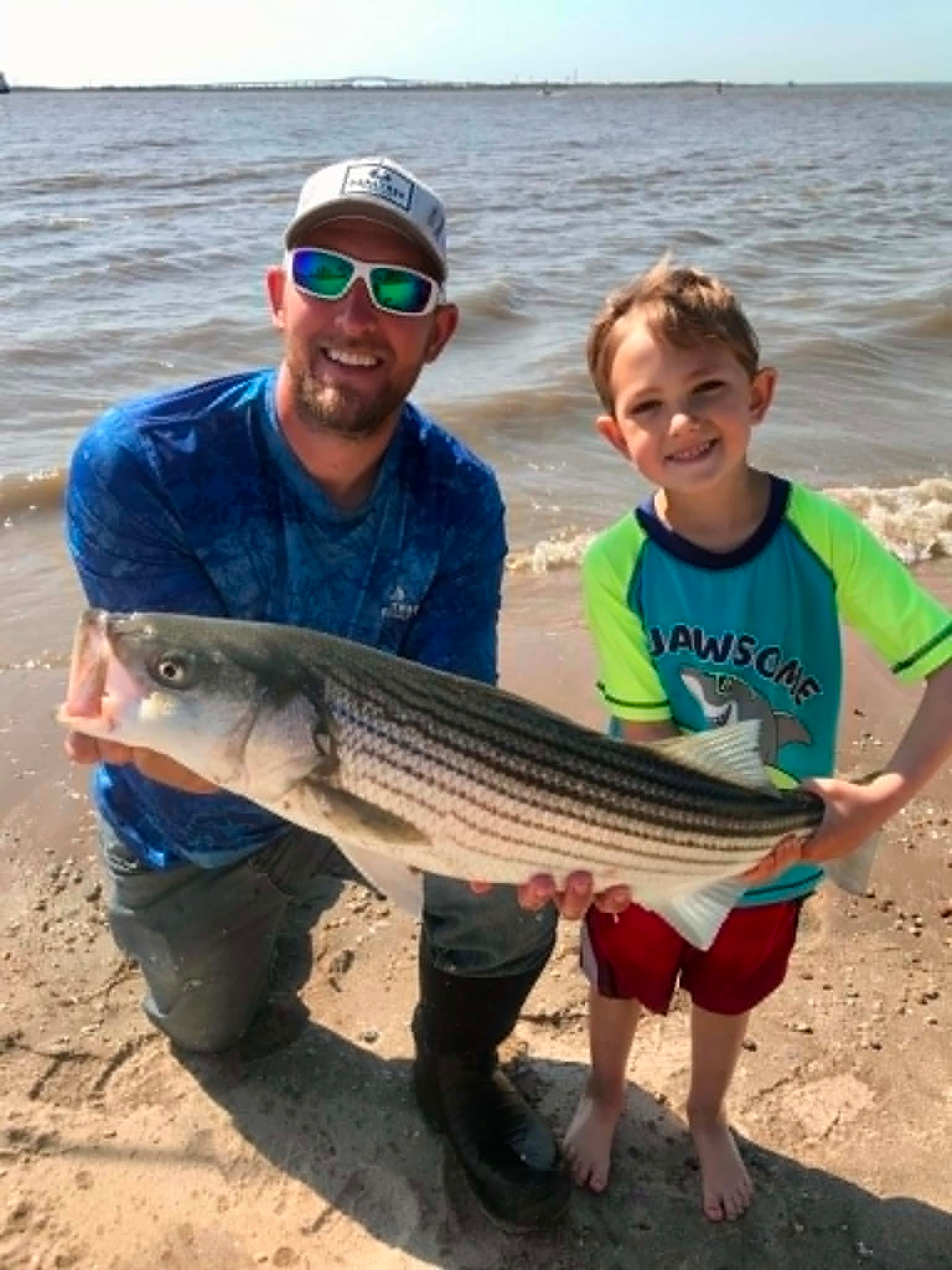 Gilch and Gauge holding a striped bass together on the beach